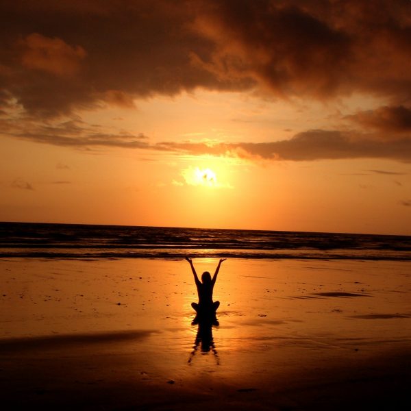 women on beach with arms up towards sky while sun sets
